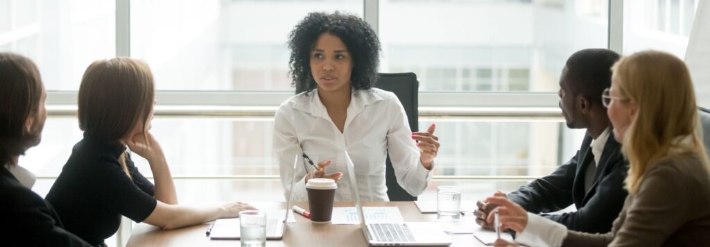 Black female boss leading corporate multiracial team meeting talking to diverse businesspeople, african american woman executive discussing project plan at group multi-ethnic briefing in boardroom